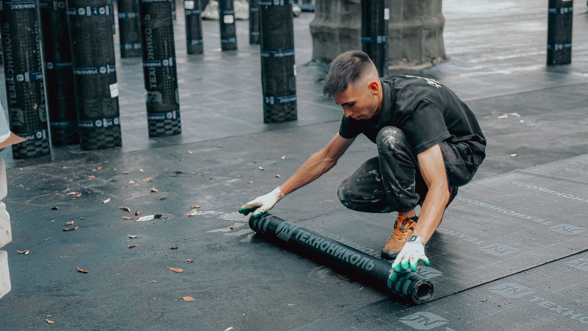 Roofer rolling out waterproofing membrane on a flat commercial roof
